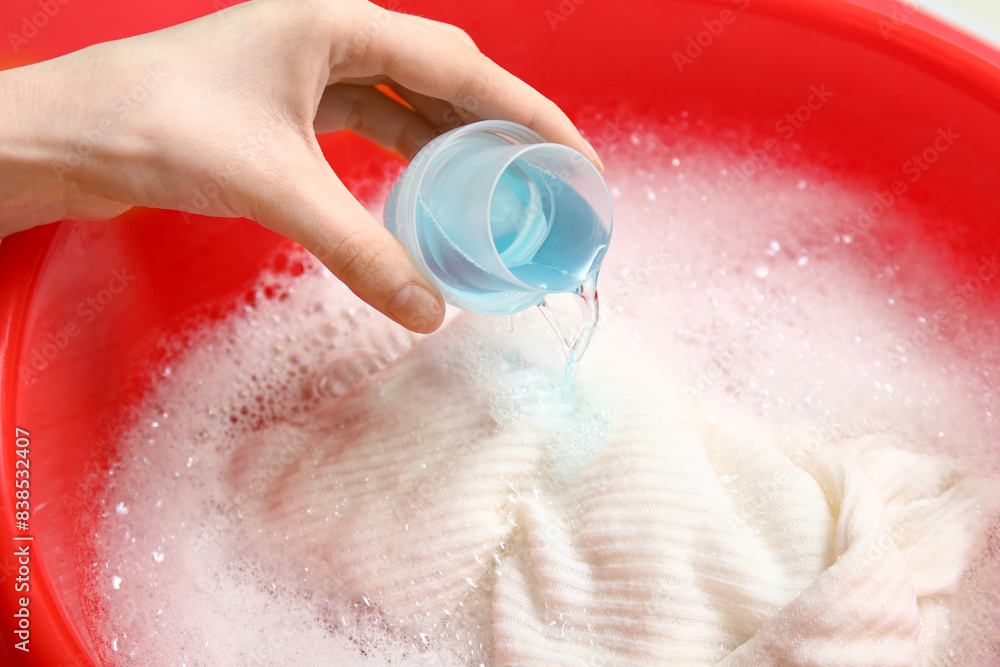 Fototapeta premium Woman adding laundry detergent to clothes in plastic basin, closeup