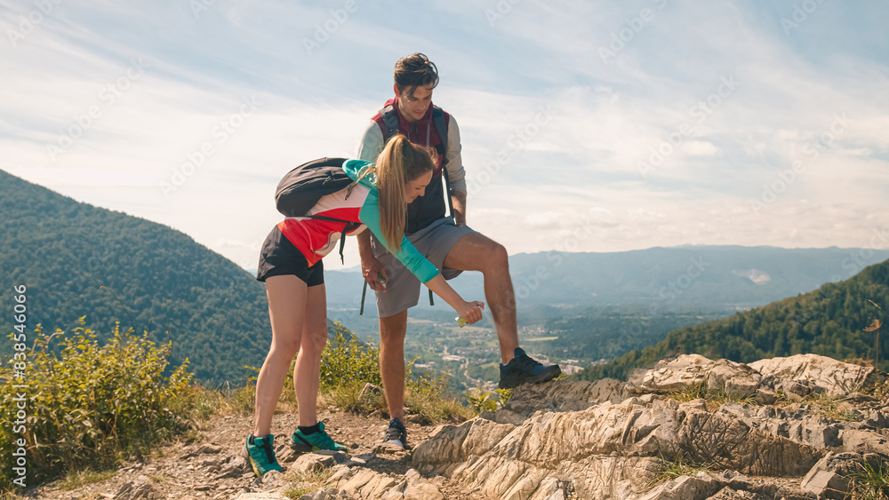 Smiling young man and a girl on a summer hiking trip, applying protection spray, a tick and mosquito repellent, with beautiful mountain scenery in the background Smiling young man and a girl on a summer hiking trip, applying protection spray, a tick and mosquito repellent, with beautiful mountain scenery in the background