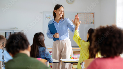 Schilderij op canvas Cheerful European female teacher giving high five to pupil girl sitting at desk