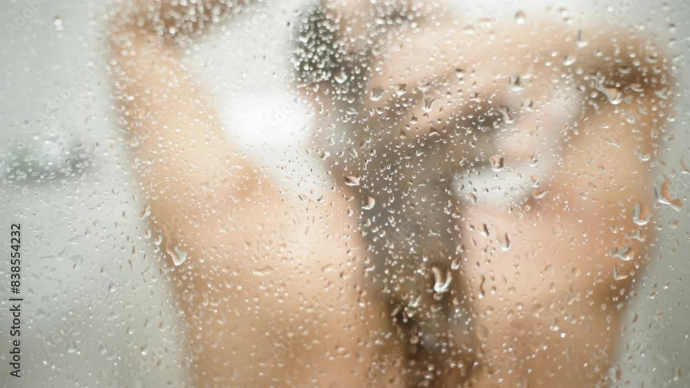 Water droplets sliding down the glass of the Shower Cabin while a Woman washes her Long Hair. Blurred background. Water droplets sliding down the glass of the Shower Cabin while a Woman washes her Long Hair. Blurred background.