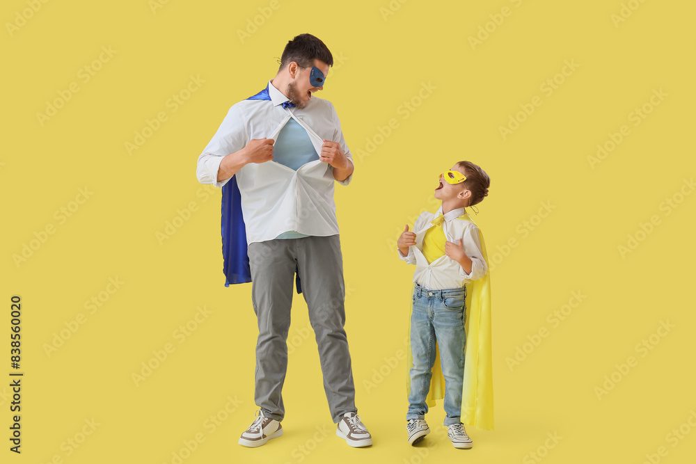 Little boy with his father in superhero costumes tearing their shirts on yellow background Little boy with his father in superhero costumes tearing their shirts on yellow background