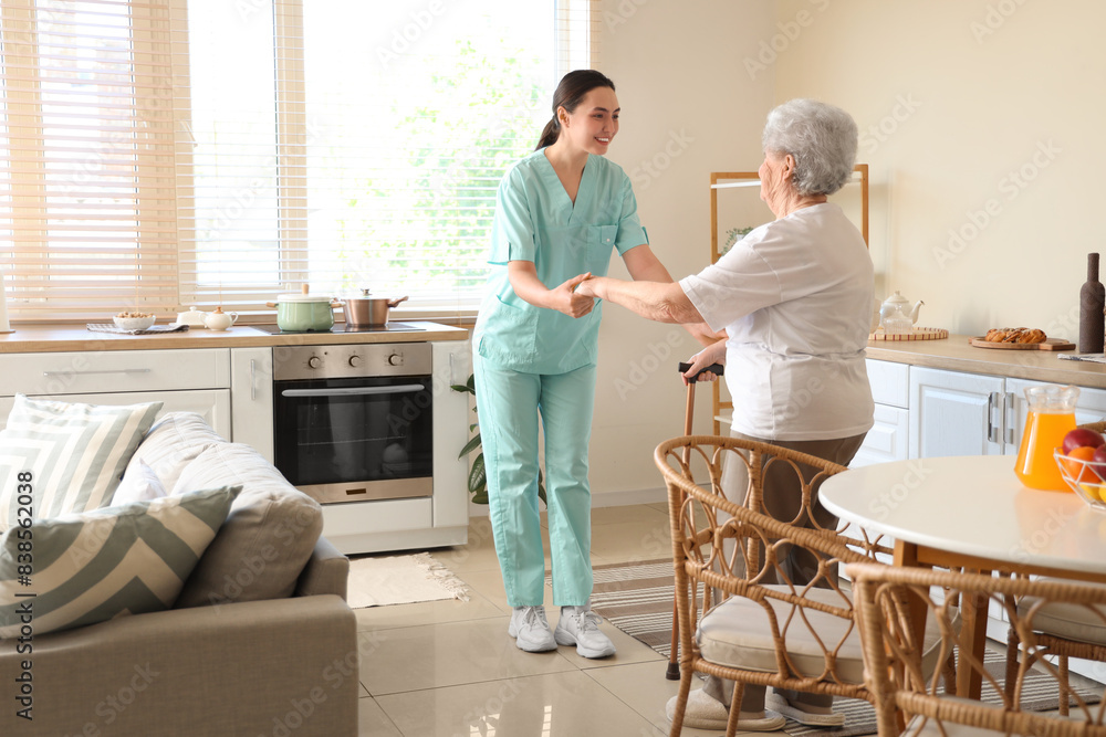 Physical therapist helping senior woman with stick to walk in kitchen Physical therapist helping senior woman with stick to walk in kitchen