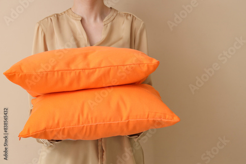 Woman with bright orange pillows on beige background, closeup