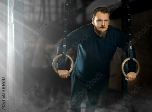 Sportive young man training with gym rings in sports hall during crossfit workout photo