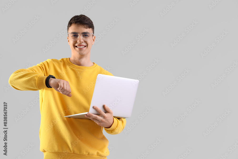 Young man with laptop checking smartwatch on light background Young man with laptop checking smartwatch on light background