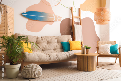 Stylish interior of living room with grey sofa, armchair, coffee table and surfboard