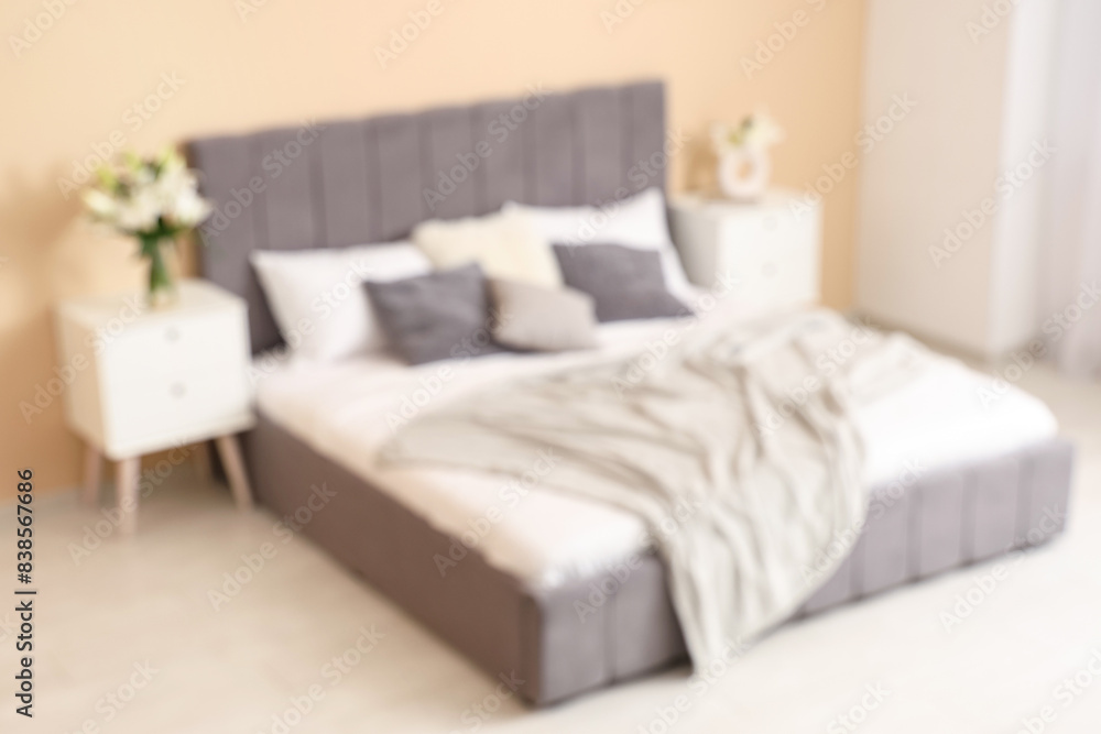 Interior of bedroom with vases of lily flowers on bedside tables near comfortable bed, blurred view Interior of bedroom with vases of lily flowers on bedside tables near comfortable bed, blurred view