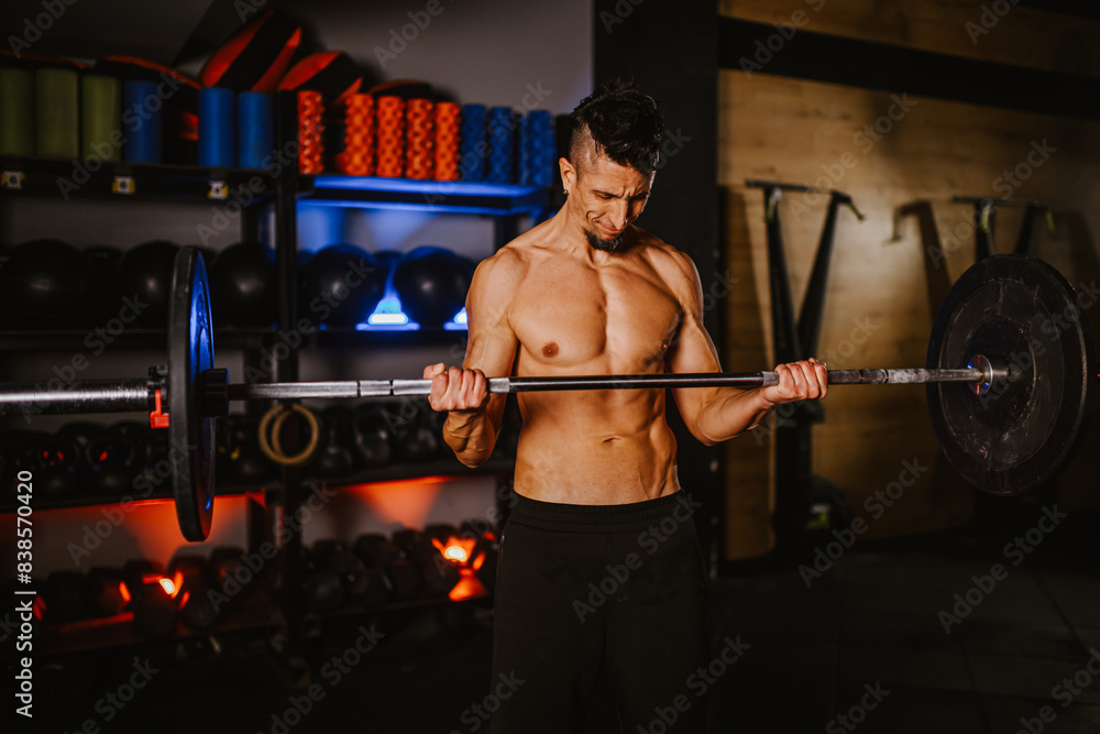 Portrait of a shirtless man exercising while lifting heavy weights in a gym Portrait of a shirtless man exercising while lifting heavy weights in a gym