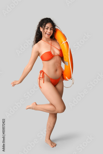 Beautiful young African-American woman in stylish orange swimsuit with lifebuoy on grey background