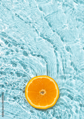 Orange fruit slice flowing on blue rippled water background. Summer fruity concept. 