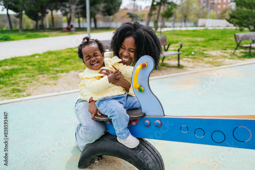 A woman and a child are sitting on a swing a public park
