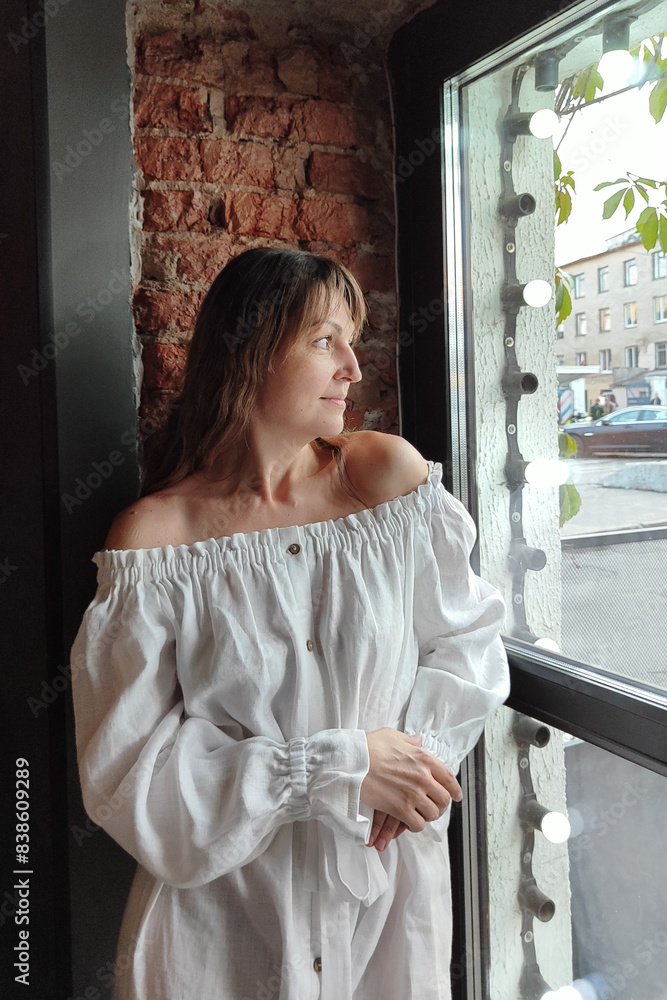 Fototapeta premium a beautiful woman with dark hair, wearing a long white dress in a city street cafe. happy people