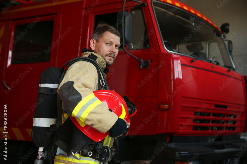 Firefighter in uniform with helmet near red fire truck at station Firefighter in uniform with helmet near red fire truck at station