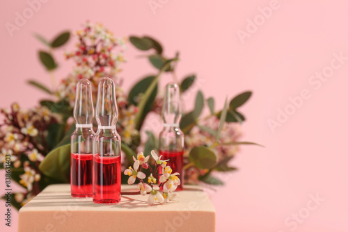 Stylish presentation of skincare ampoules and flowers on pink background, closeup. Space for text