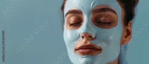 Close-up of a woman with a blue face mask, eyes closed, relaxing against a blue background, showcasing a spa skincare routine.