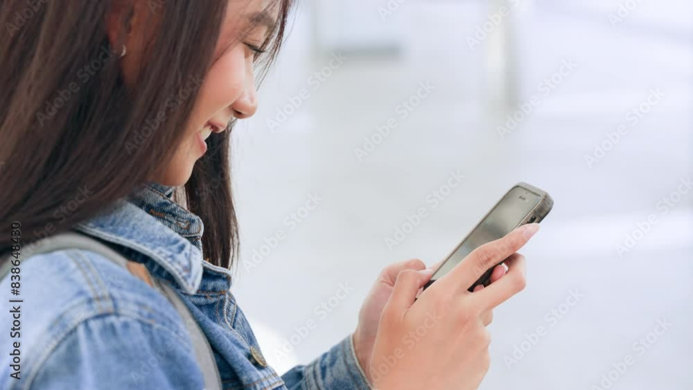 Young asian woman smiling using mobile smart phone outdoor. Happy female tourist wearing jeans jacket and holding smartphone at public Young asian woman smiling using mobile smart phone outdoor. Happy female tourist wearing jeans jacket and holding smartphone at public