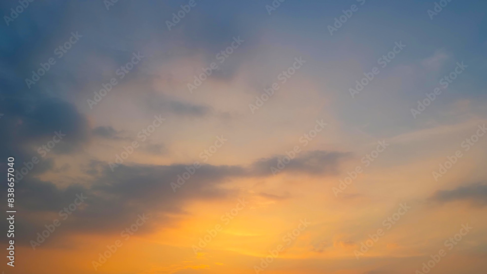 A serene sunset with the sky painted in soft hues of orange and yellow near the horizon. Dark clouds add depth and contrast to the warm tones, creating a peaceful ambiance. Sunset sky background.

