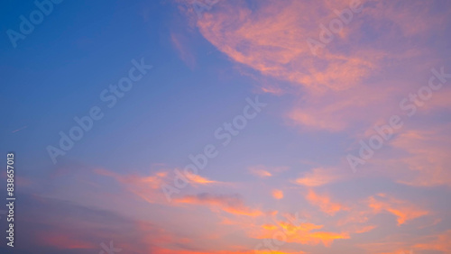 A beautiful sunset with soft, pink-tinged clouds spread across a gradient sky. The sky transitions from a deeper blue at the top to a warmer, lighter hue near the horizon. Cloud background. 