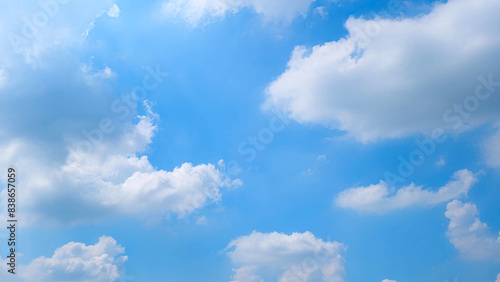A serene blue sky filled with fluffy white clouds scattered across the expanse. The sunlight illuminates the scene  creating a peaceful and uplifting atmosphere. Nature s beauty background. 