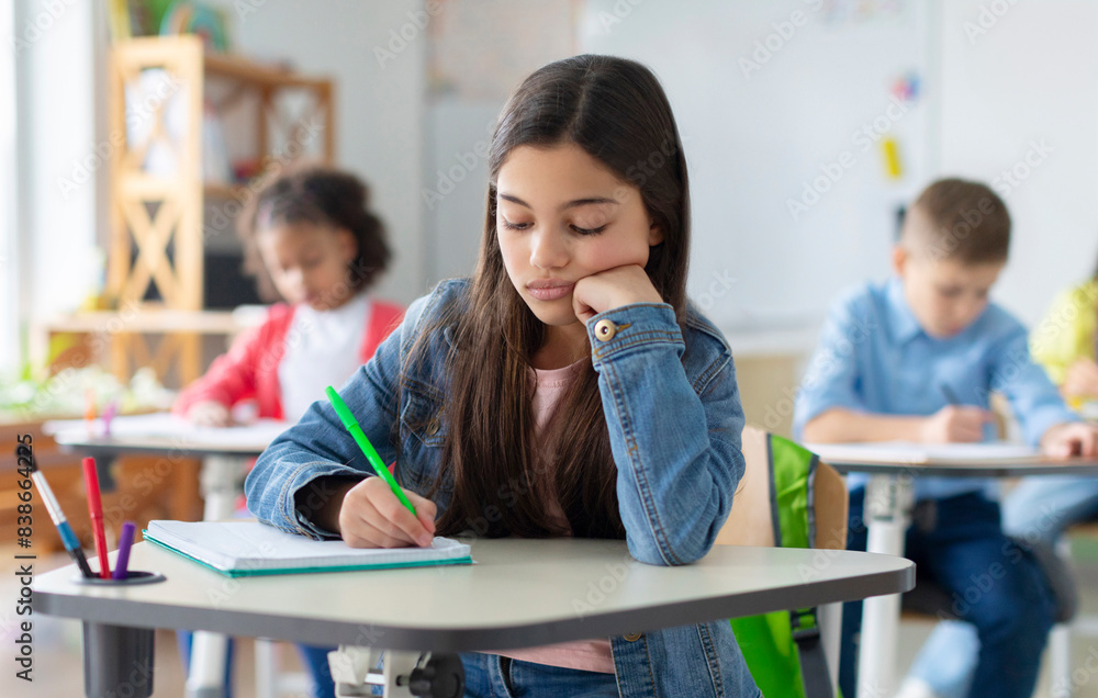© Home-stock - Tired and bored schoolgirl sitting at desk in classroom at school, writing in her notebook and thinking, resting head on hand © Home-stock - Tired and bored schoolgirl sitting at desk in classroom at school, writing in her notebook and thinking, resting head on hand