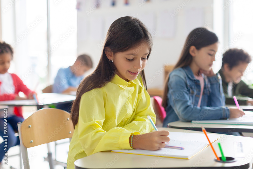 Busy European student girl concentrated on quiz filling blank or writing test, sitting at desk in classroom interior Busy European student girl concentrated on quiz filling blank or writing test, sitting at desk in classroom interior