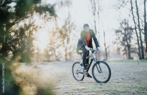 A man in casual wear rides his bicycle through a lush park, basking in the afternoon sun, embodying relaxation and a healthy lifestyle. Blurred photo.