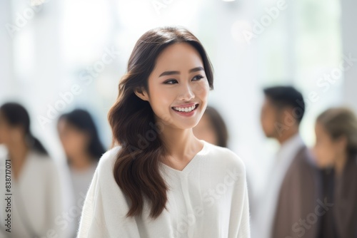 Dialogue unfolds as Asian woman, clad in white business attire, engages in conversation amid bustling public space backdrop, her demeanor poised and engaged.