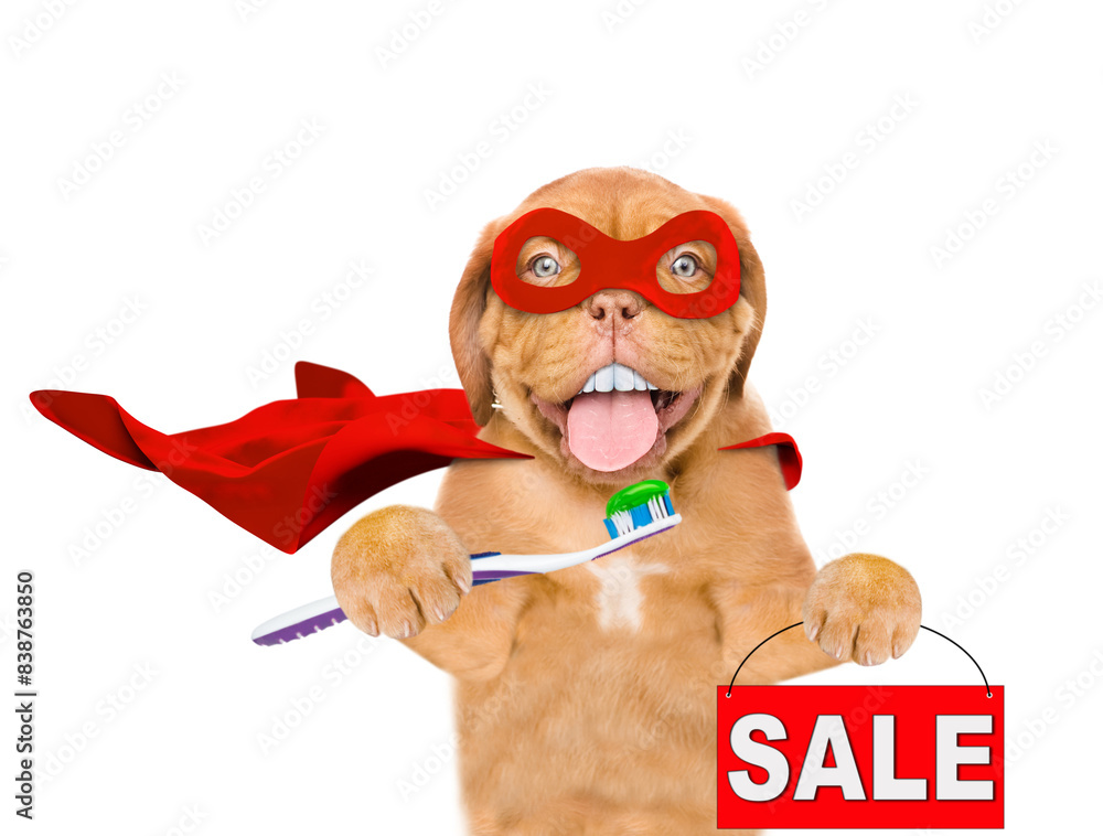 Φωτογραφία Happy Mastiff puppy with big funny teeth wearing superhero costume showing signboard with labeled sale and holding toothbrush  with toothpaste in it paw