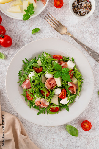 Fresh summer salad with arugula, melon, prosciutto and mozzarella cheese on concrete background, Healthy food. Top view.