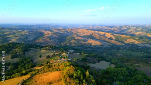 Calm aerial pullback and pan right shot from Penna San Giovanni (MC) with brown fields, thickets, buildings, roads, partly lit and partly shaded from the precious golden hour sunlight, in hillscapes photo