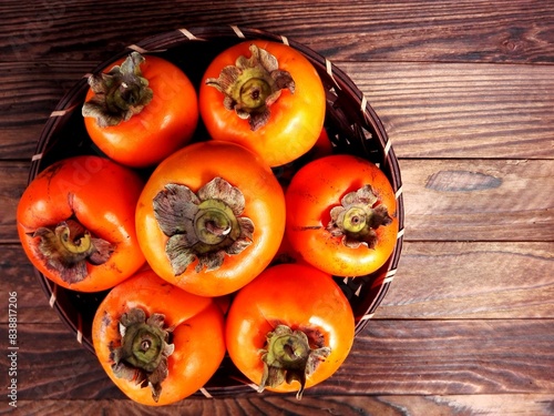 Persimmon kaki fruit basket on wooden background top view. Tasty persimmon fruit or kaki wicker basket closeup. Organic fresh persimmon from fuyu fruit garden farm. Raw orange diospyros kaki close up