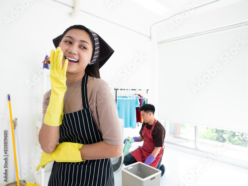 Asian family couple in a bright laundry room wearing aprons and gloves enjoying their time together while doing household chore and wife laughing husband when use washing machine