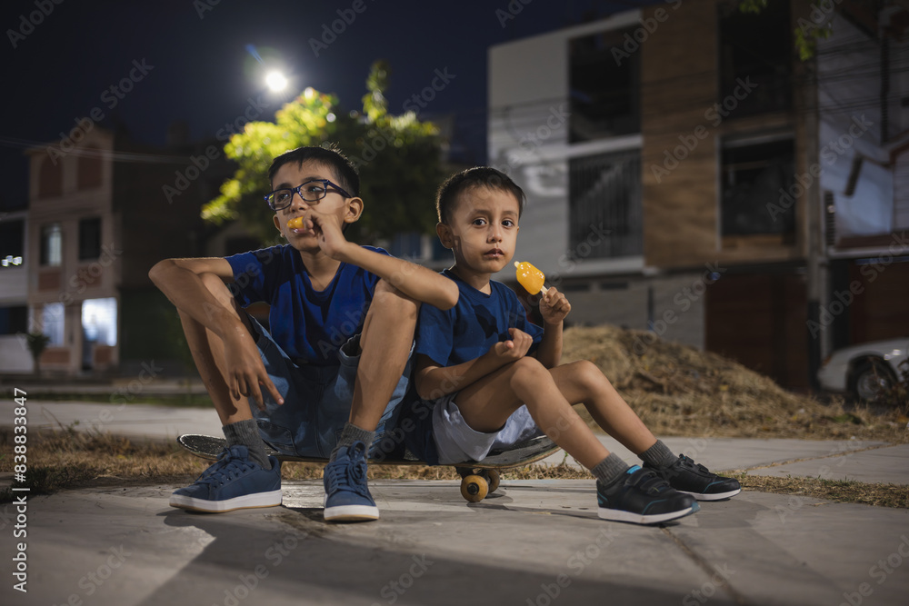 Obraz premium Boys eating popsicles while sitting on skateboard at night summer