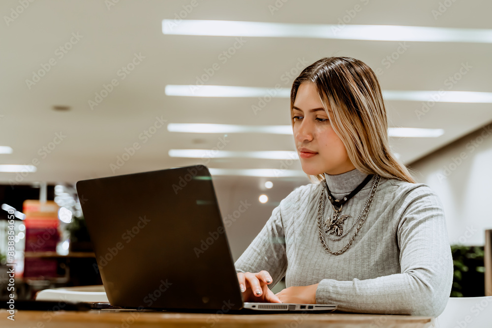 Empowered blonde-haired Latina woman working with her laptop at a coworker. Self-employed and entrepreneur. Financially independent. Empowered blonde-haired Latina woman working with her laptop at a coworker. Self-employed and entrepreneur. Financially independent.