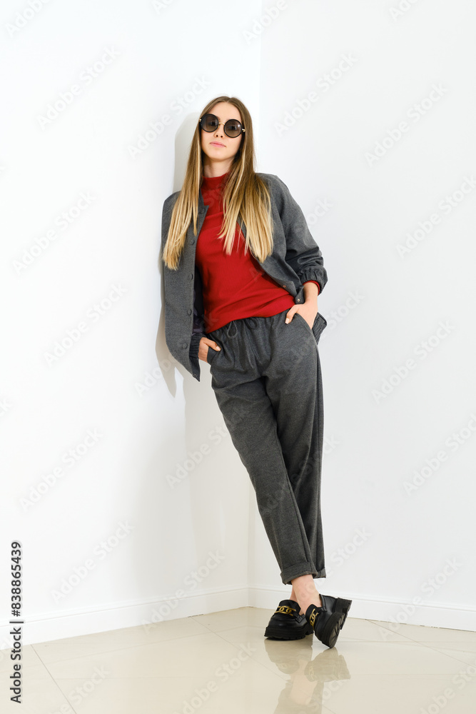 Woman in casual grey sportive clothes and red turtleneck leaning against white wall Woman in casual grey sportive clothes and red turtleneck leaning against white wall