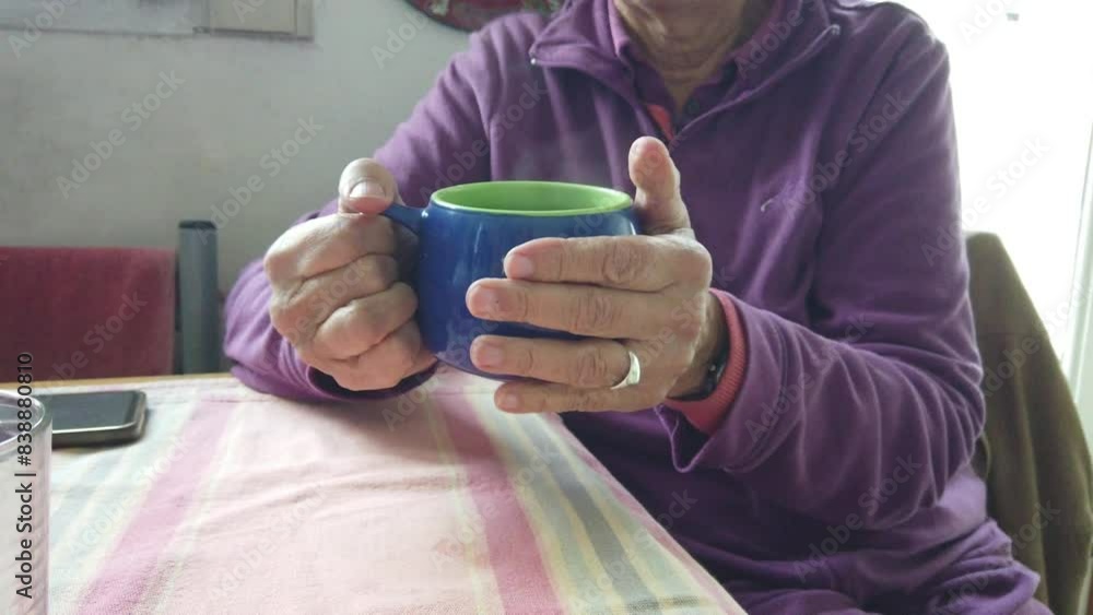 White hands of senior woman holds a hot smoking mug drinking it at homey table White hands of senior woman holds a hot smoking mug drinking it at homey table