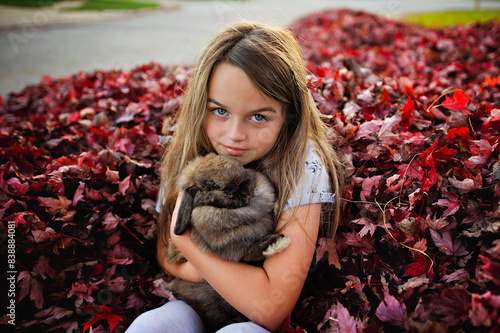 Beautiful young girl holding Holland Lop rabbit in red leaves photo