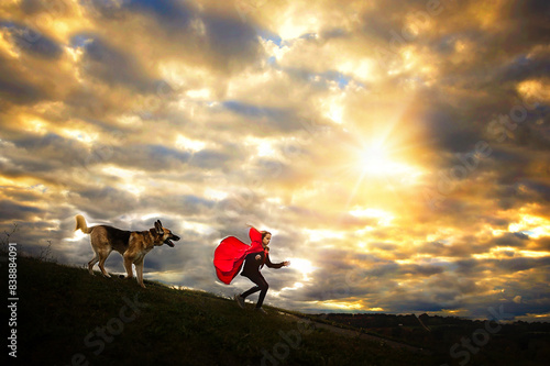 Young girl in red cape running from German Shepherd photo