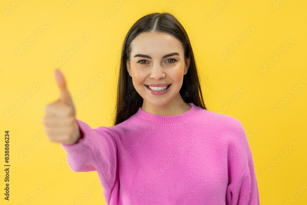 Charming happy woman with positive smile showing thumb up gesture while posing over yellow studio background Charming happy woman with positive smile showing thumb up gesture while posing over yellow studio background