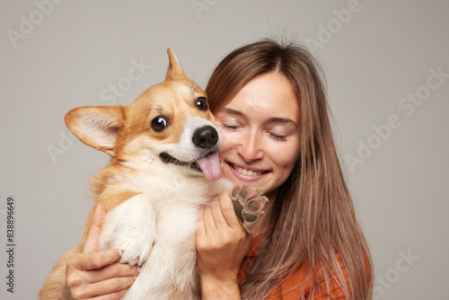 Canvas Print a brunette girl holds and hugs a red corgi dog on a clean light background, the