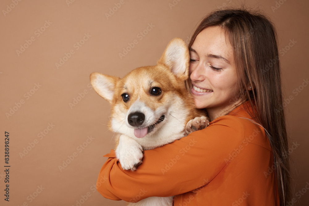 Girl hugging Pembroke Welsh Corgi on a beige clean background in the studio, love for animals Girl hugging Pembroke Welsh Corgi on a beige clean background in the studio, love for animals