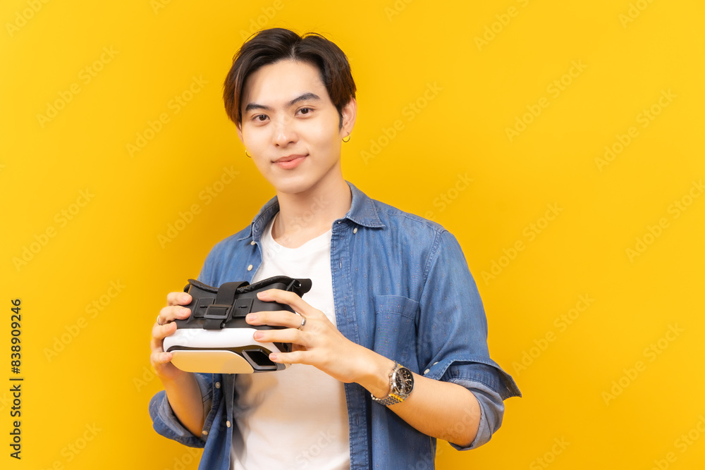 Asian young man in jacket jean and playing video games using vr with headphones on yellow background isolated. Asian young man in jacket jean and playing video games using vr with headphones on yellow background isolated.