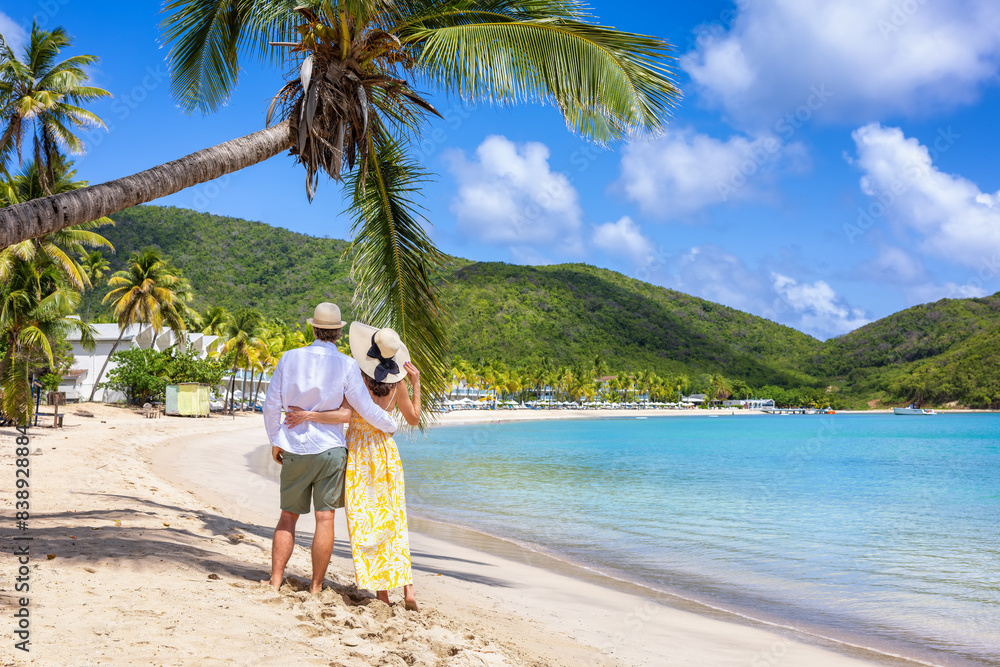 Happy holiday couple with sunhats enjoys a tropical beach with palm trees surrounded by rain forest in the Caribbean, Antigua island Happy holiday couple with sunhats enjoys a tropical beach with palm trees surrounded by rain forest in the Caribbean, Antigua island