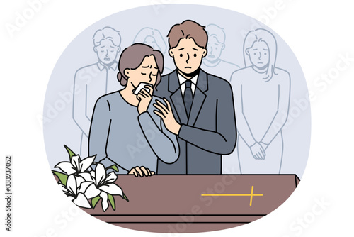 People at funeral ceremony stand near coffin with catholic cross and mourn deceased to say farewell. Upset friends and relatives at church service before funeral of man of christian faith