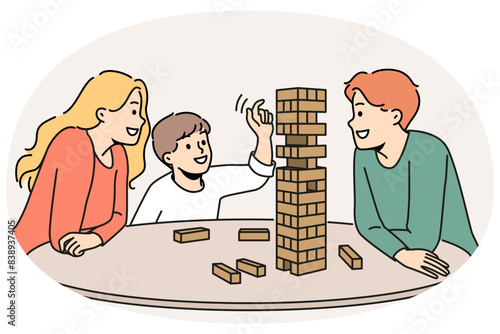 Happy family plays jenga with child enjoying board game and developing fine motor skills in baby. Satisfied boy plays jenga with parents pulling wooden block out of unstable tower.