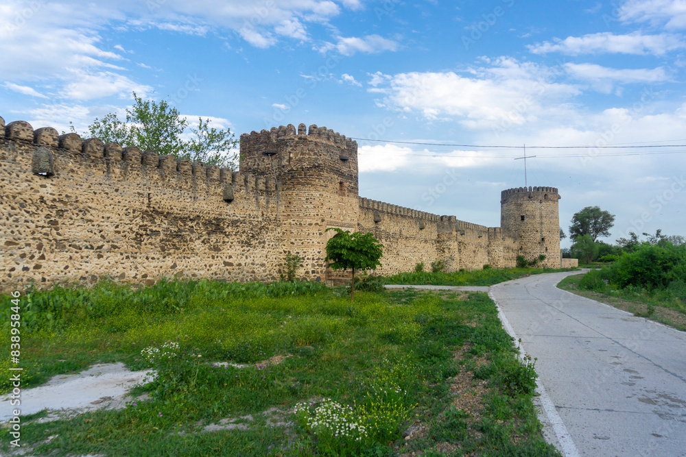 Wall with loopholes and towers of the Kolagiri fortress. Asphalt road leading to the entrance Wall with loopholes and towers of the Kolagiri fortress. Asphalt road leading to the entrance