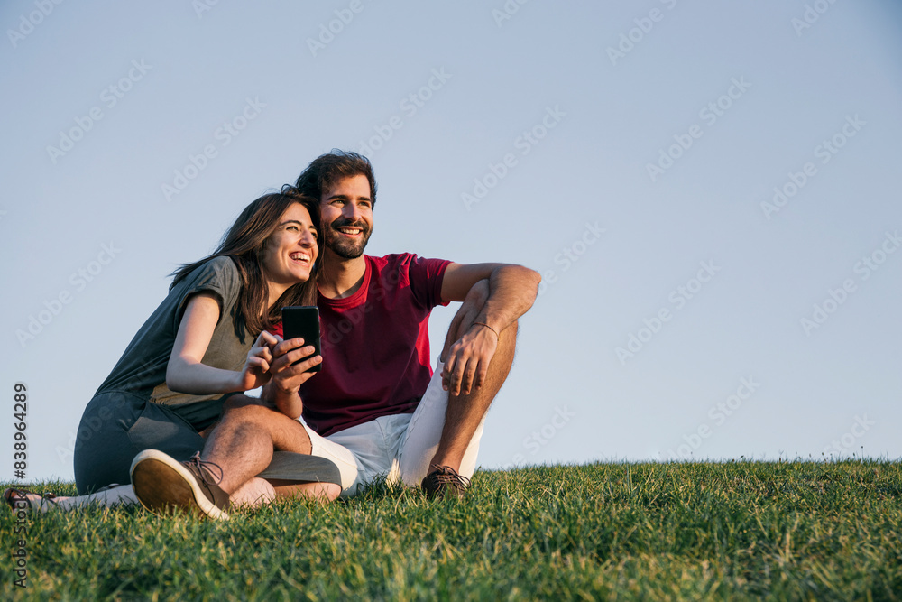 Couple sitting on grass against clear sky during sunset Couple sitting on grass against clear sky during sunset