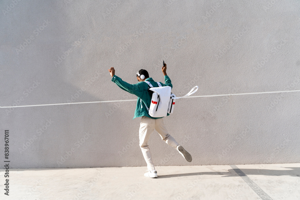 Man with backpack and headphones dancing on footpath