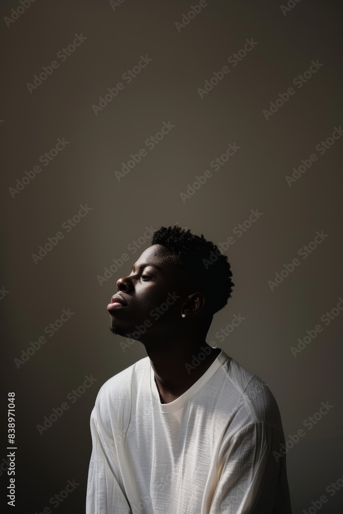 Young African American man in a white shirt, eyes closed, embracing serenity in a dark, minimalist setting, highlighting a calm and contemplative mood. Young African American man in a white shirt, eyes closed, embracing serenity in a dark, minimalist setting, highlighting a calm and contemplative mood.