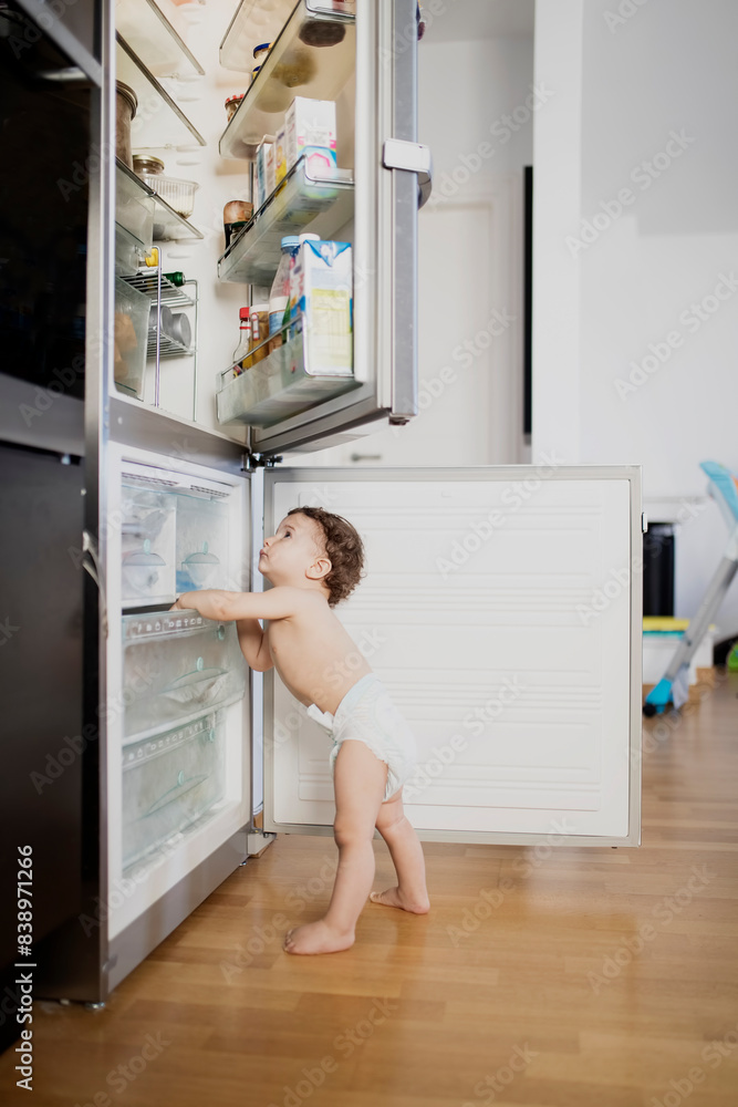 Baby boy wearing diaper exploring refrigerator in the kitchen Baby boy wearing diaper exploring refrigerator in the kitchen